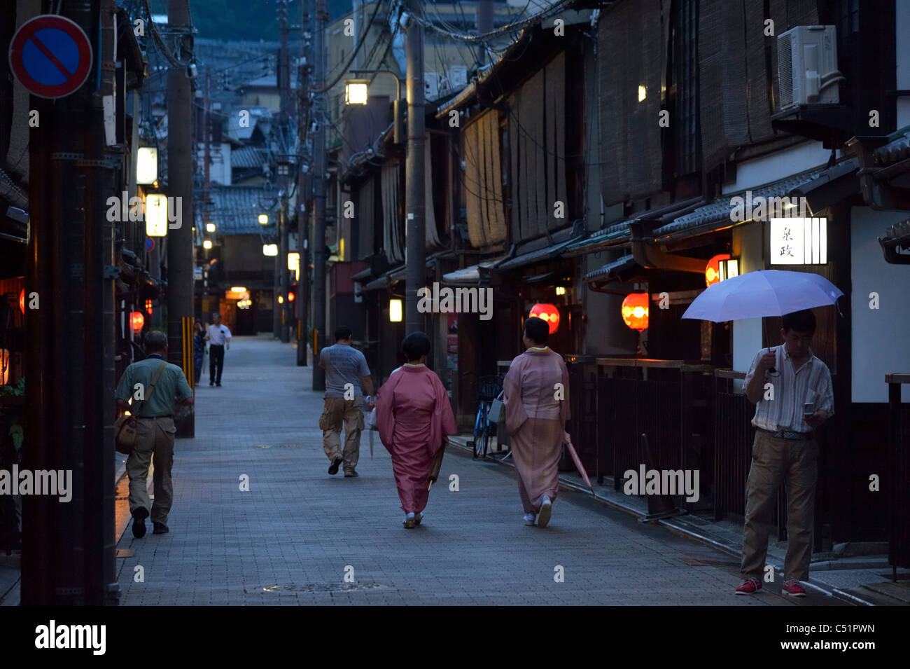 Two Japanese Geisha (Geiko) walking along traditional restaurants in the historical Gion district, Kyoto, Japan JP Stock Photo