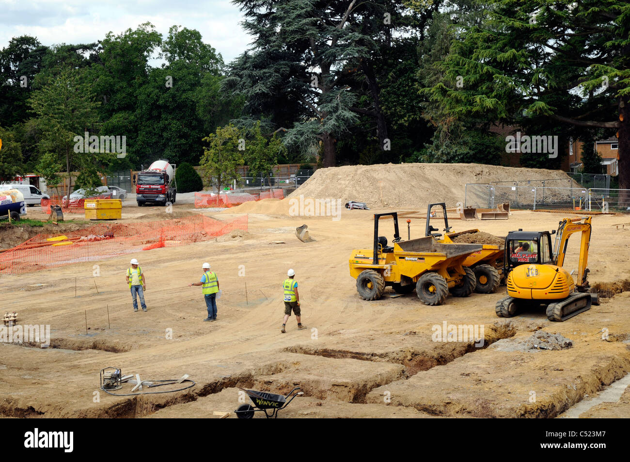 Building site showing strip foundation trenches and cement mixer delivering concrete. Stock Photo