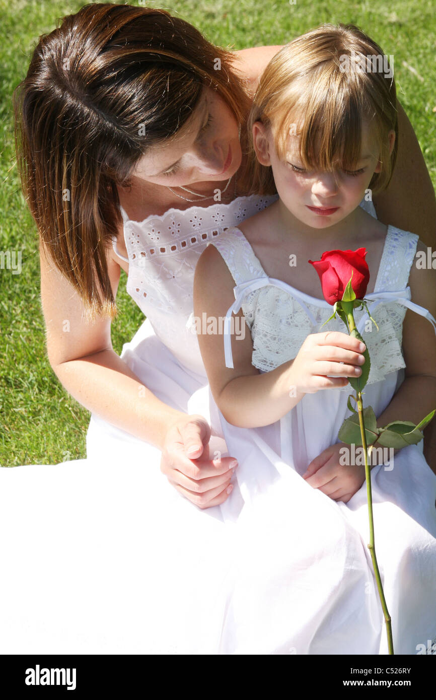 A young woman and girl in white dresses holding a red rose flower Stock ...