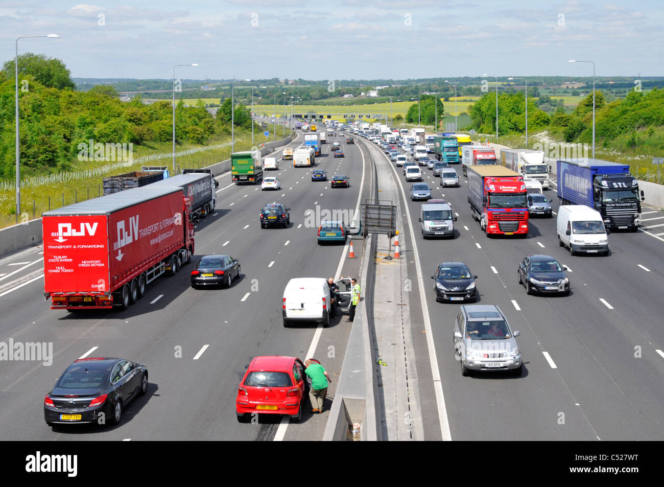 Motorway vehicles stationary in lane 4 accident involving red car below bridge (witnesses awaiting emergency services) M25 Essex England UK Stock Photo