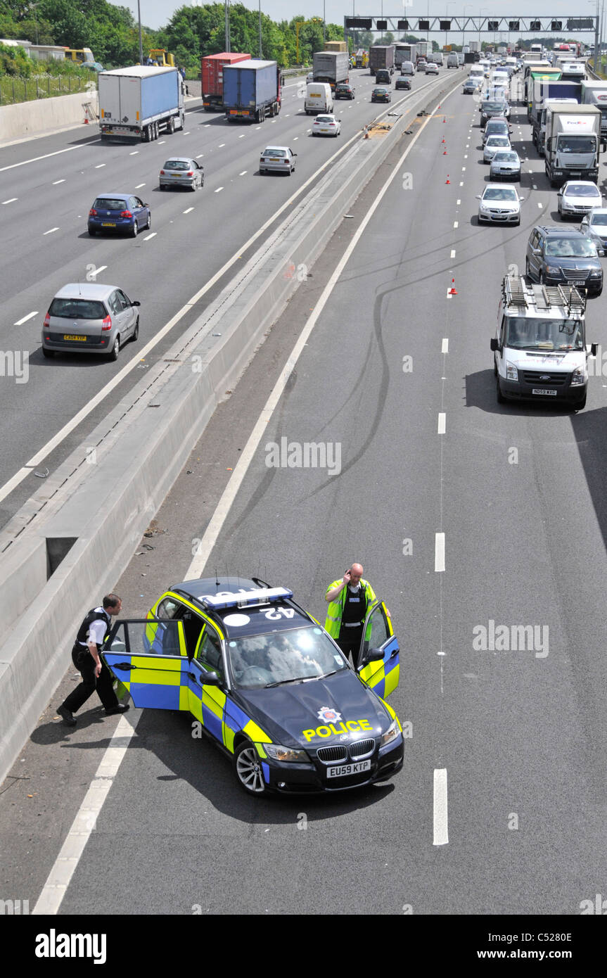 Essex police at  M25 motorway car crash accident under bridge parking in lane 4 with skid marks beyond into concrete crash barrier traffic jam UK Stock Photo