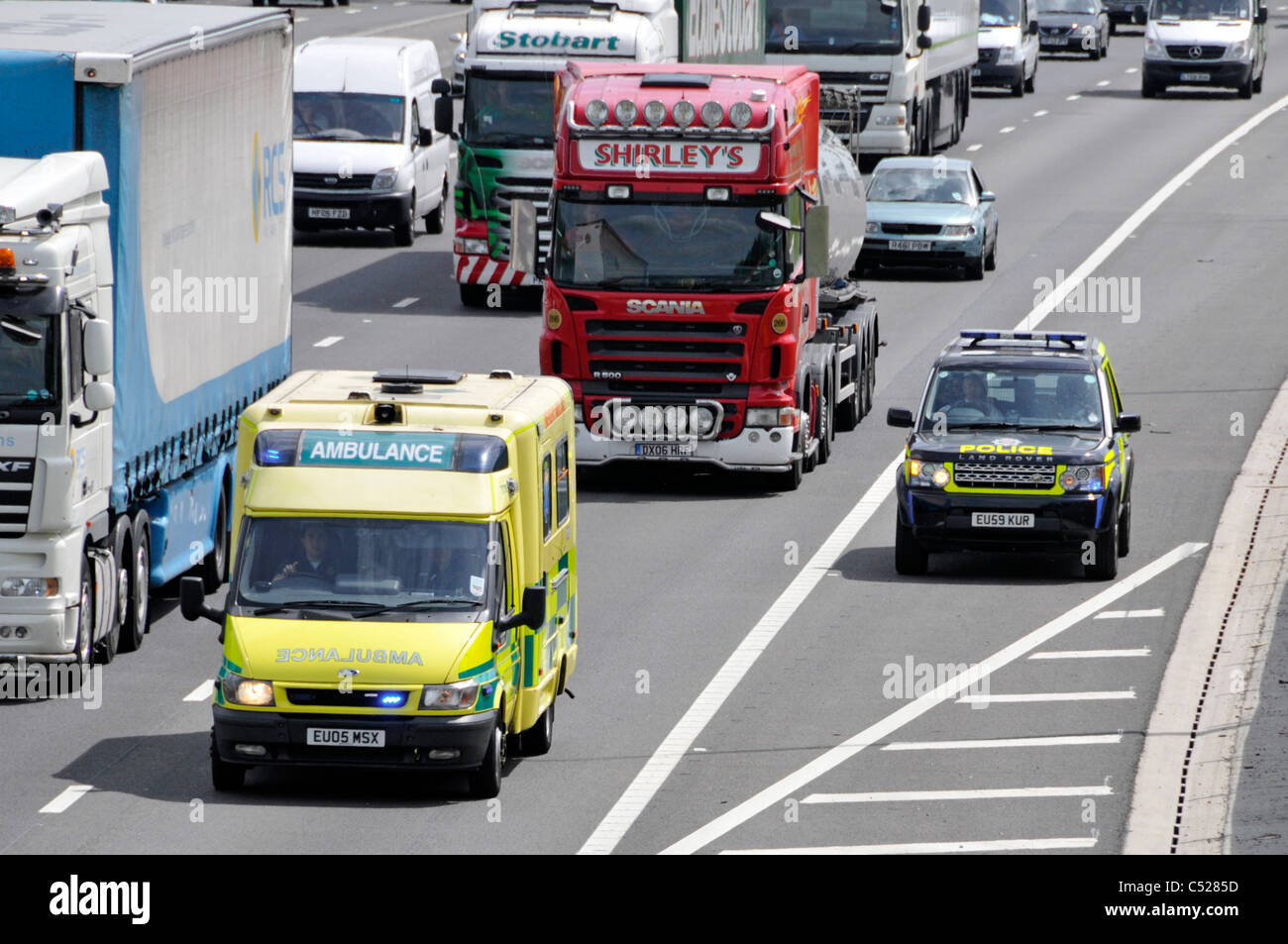 Emergency services lights on ambulance & police driver heavy motorway traffic on way to accident using lane one & hard shoulder M25 Essex England UK Stock Photo