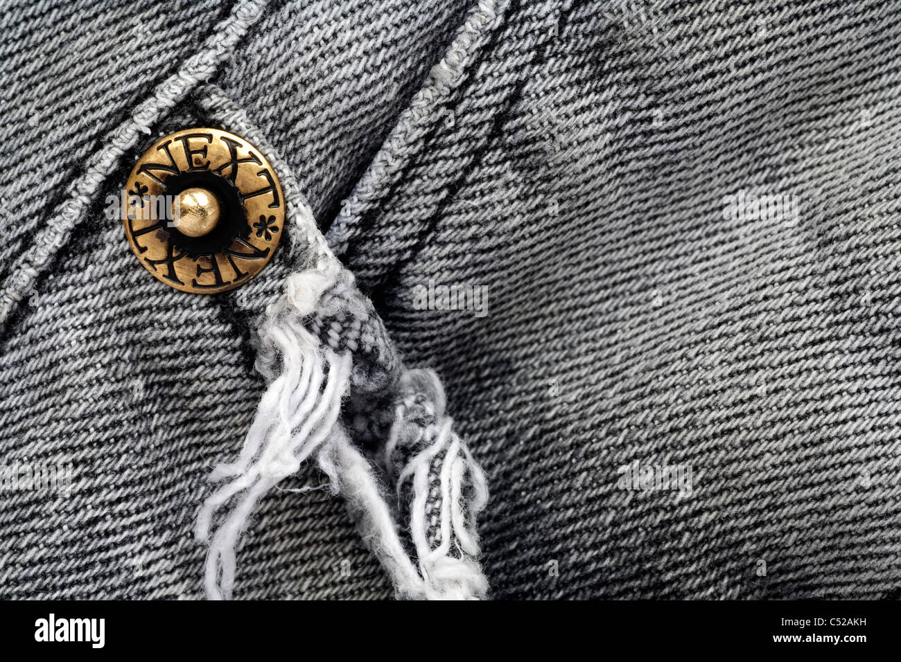Detail of the pocket area and metal stud on a pair of faded and worn Next grey (gray) denim jeans Stock Photo