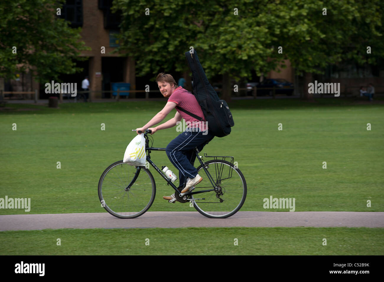 Cambridge. Young Man on bicycle and musical instrument crossing Parkers