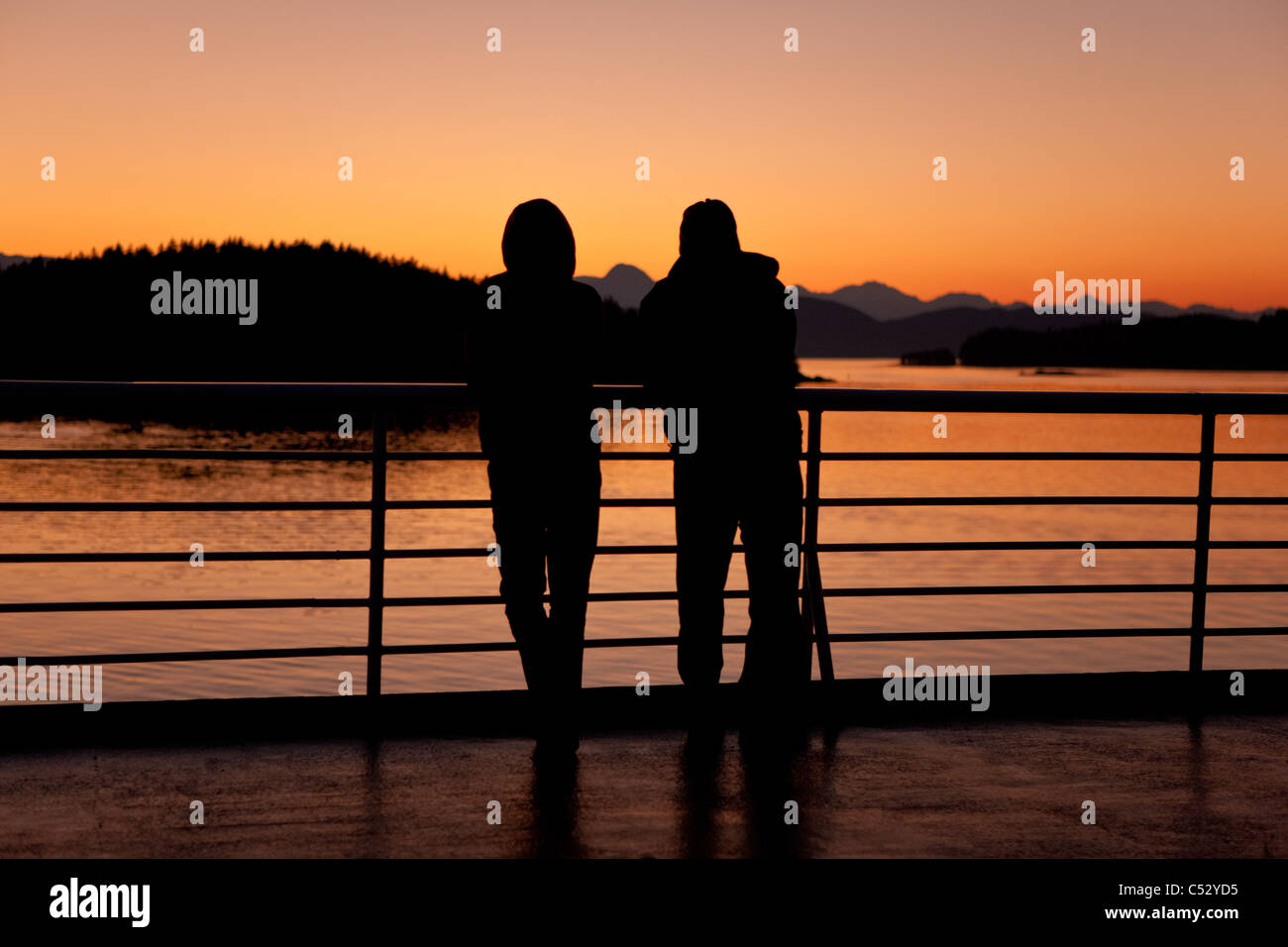 A couple watches the sunset from the deck of the M/V Matanuska as it  heads for Auke Bay near Juneau, Southeast Alaska, Autumn Stock Photo