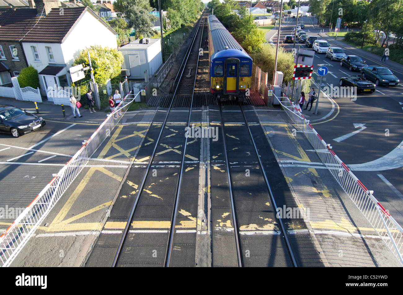 cars cross a level crossing with barriers down as train passes through Stock Photo