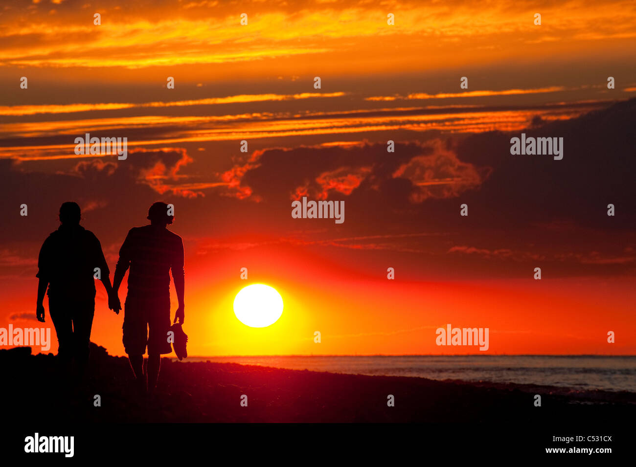 Couple walking hand in hand along a beach at sunset, on the Norfolk ...