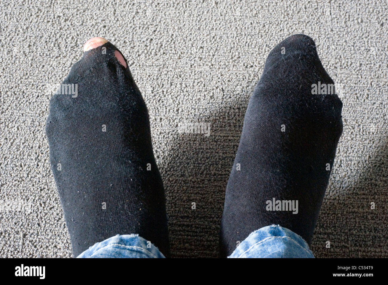 man wearing black socks one with hole in and toe poking through Stock