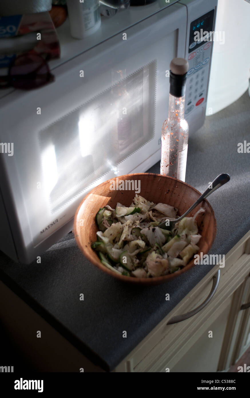 Sunlight on a salad in a wooden bowl with a bottle of dressing in a kitchen near the microwave Stock Photo