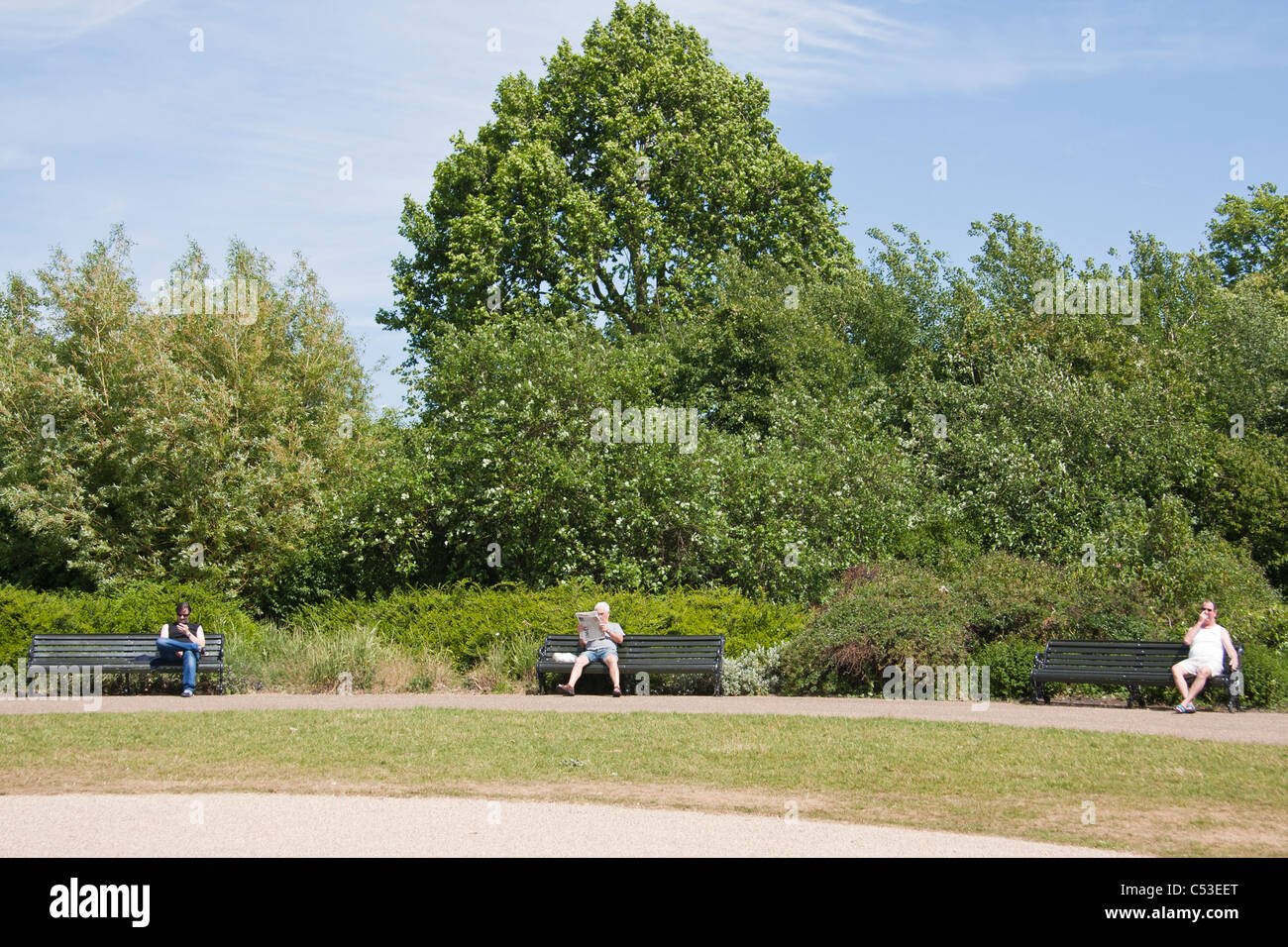 Three people sitting on three benches on a park Stock Photo