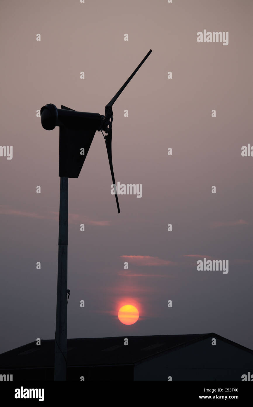 setting sun seen against silhouette of a small commercial wind turbine ...