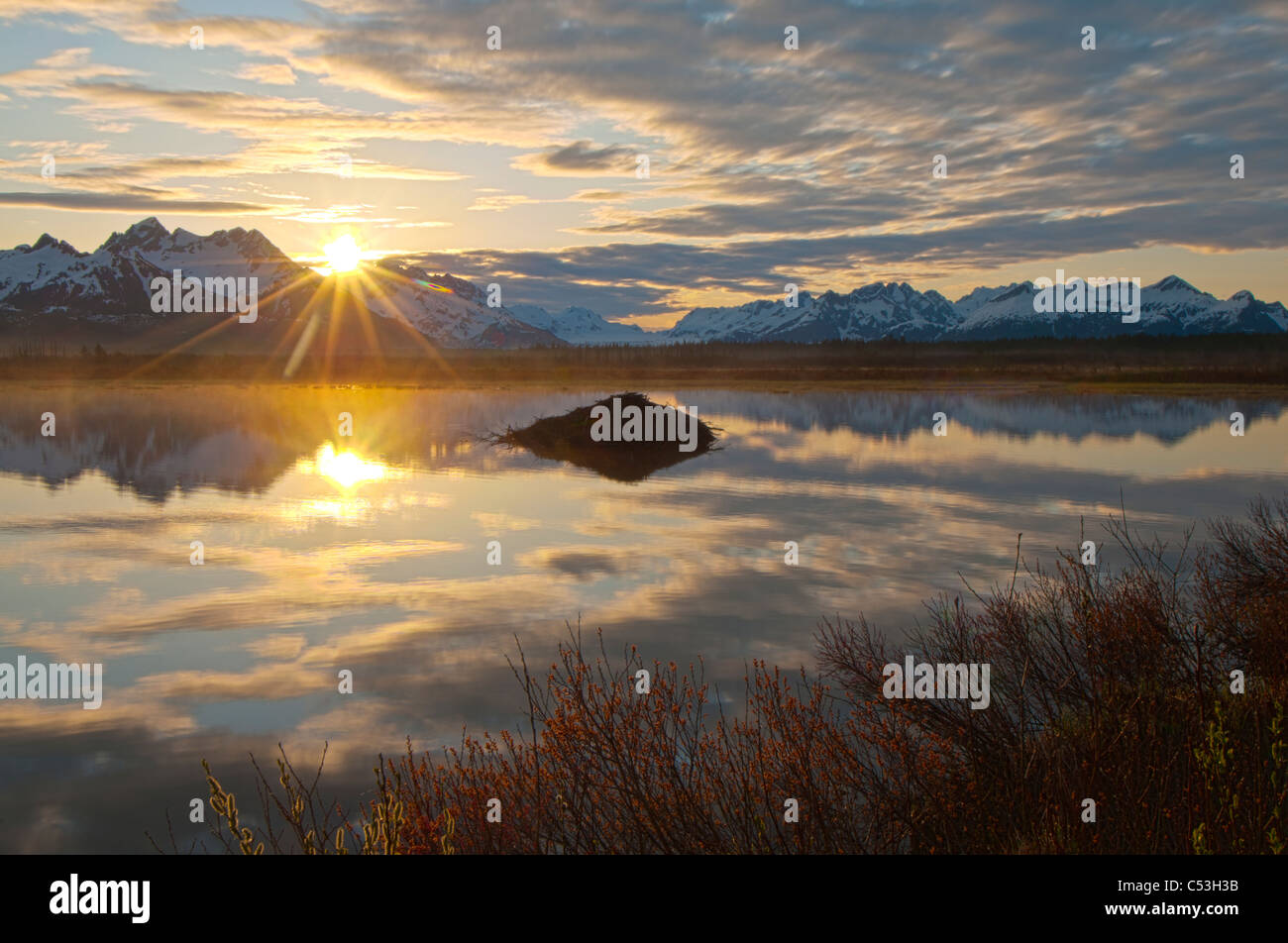 Sun rises over the Chugach Mountains with a pond and beaver lodge in the foreground, Chugach National Forest, Alaska Stock Photo