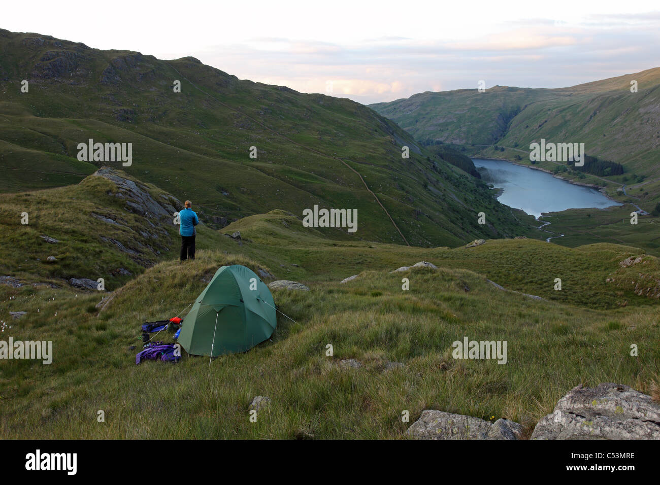 Hill Walker with Tent Enjoying the View Over Haweswater Reservoir from a Wild Camp Near Small Water Lake District Cumbria UK Stock Photo