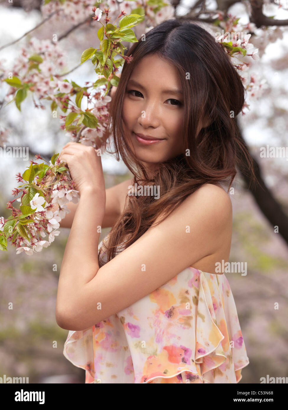 Portrait of a beautiful young smiling Asian woman standing at a blooming cherry tree in a park Stock Photo