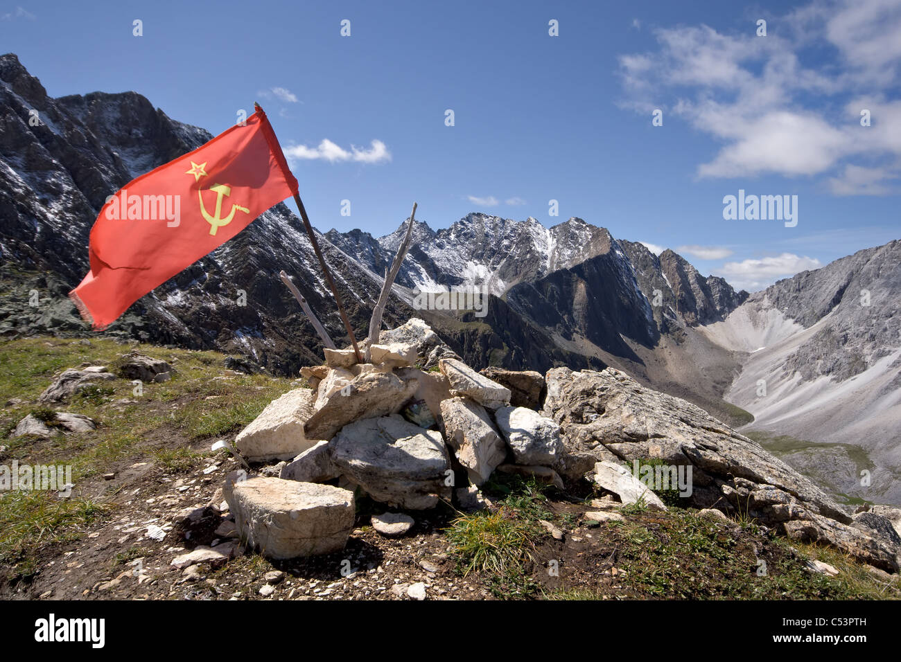 Red USSR flag at the top of mountain among stones against rocks and blue sky. East Sayan Mountains. Buryat Republic. Russia. Stock Photo