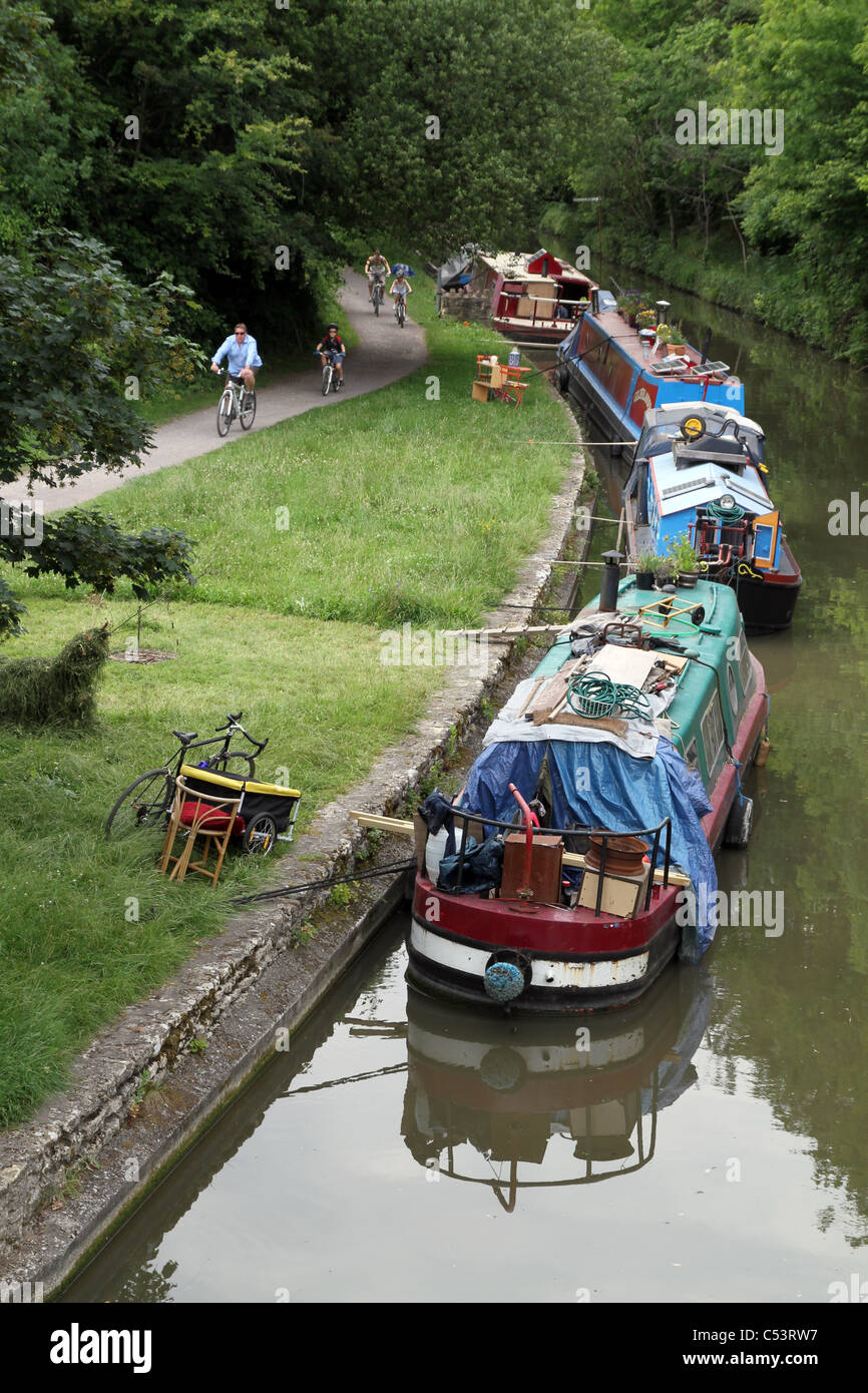 PEOPLE WALK AND CYCLE PAST BARGES ALONG THE KENNET AND AVON CANAL IN WILTSHIRE, ENGLAND, UK Stock Photo