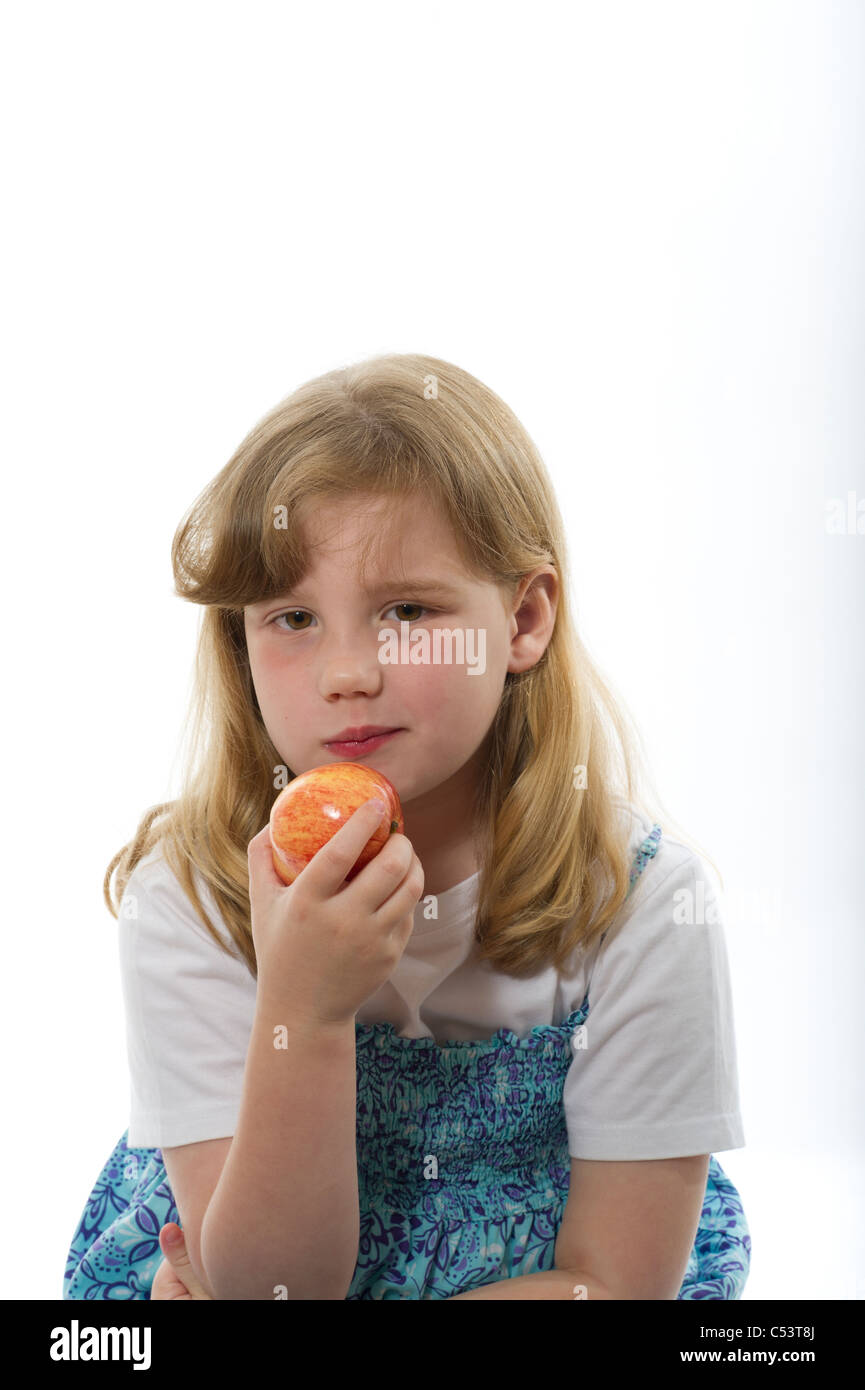 A young girl 8 years eating an apple against a plain white studio background. Stock Photo