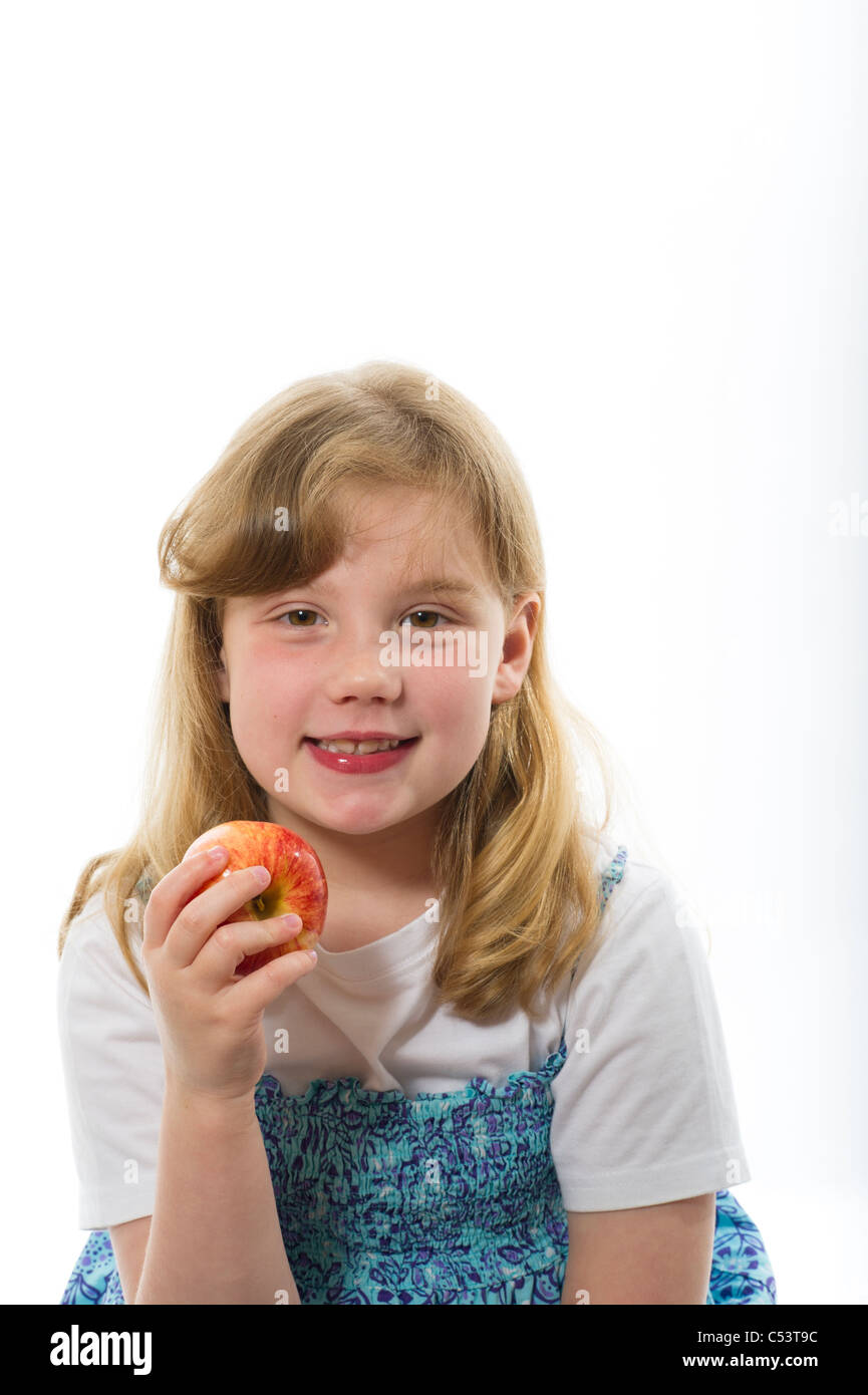 A young girl 8 years eating an apple against a plain white studio background. Stock Photo