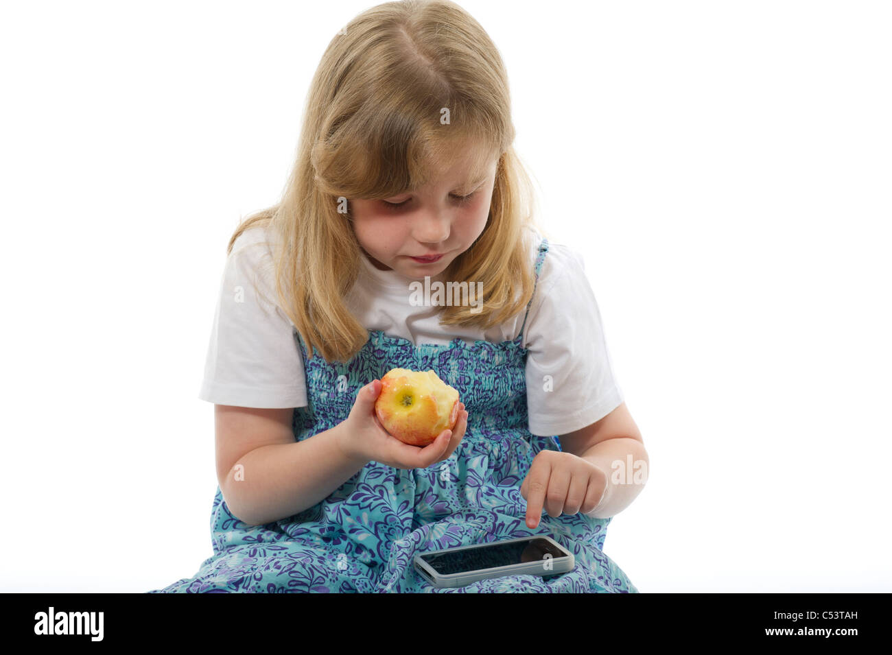 A young girl eight years playing with ipod/iphone while eating an apple against plain white studio background. Stock Photo