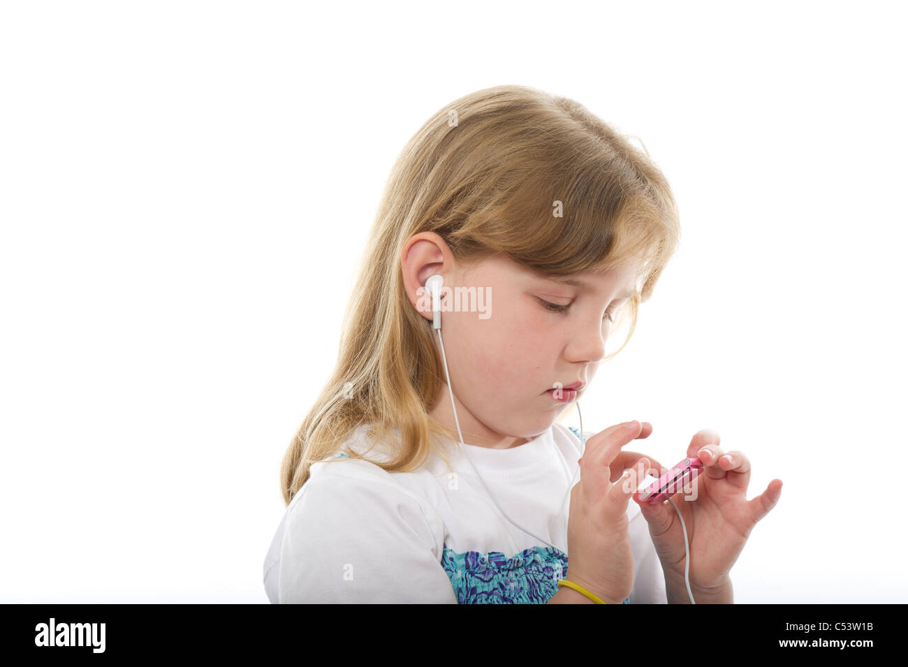 A young girl wearing ear buds listening to an MP3 (ipod Nano) shot against a plain white background. Stock Photo