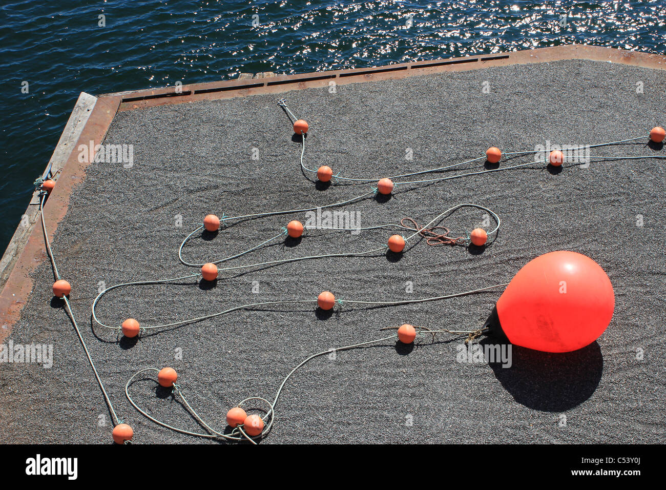 Red buoy laying on the ground besides waterway Stock Photo