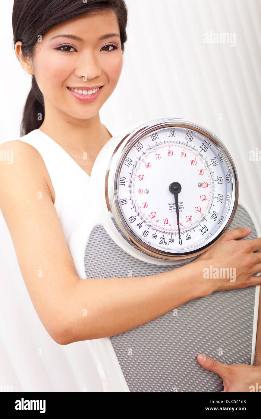 Happy & beautiful Oriental Asian Chinese woman holding weighing scales at gym or health club