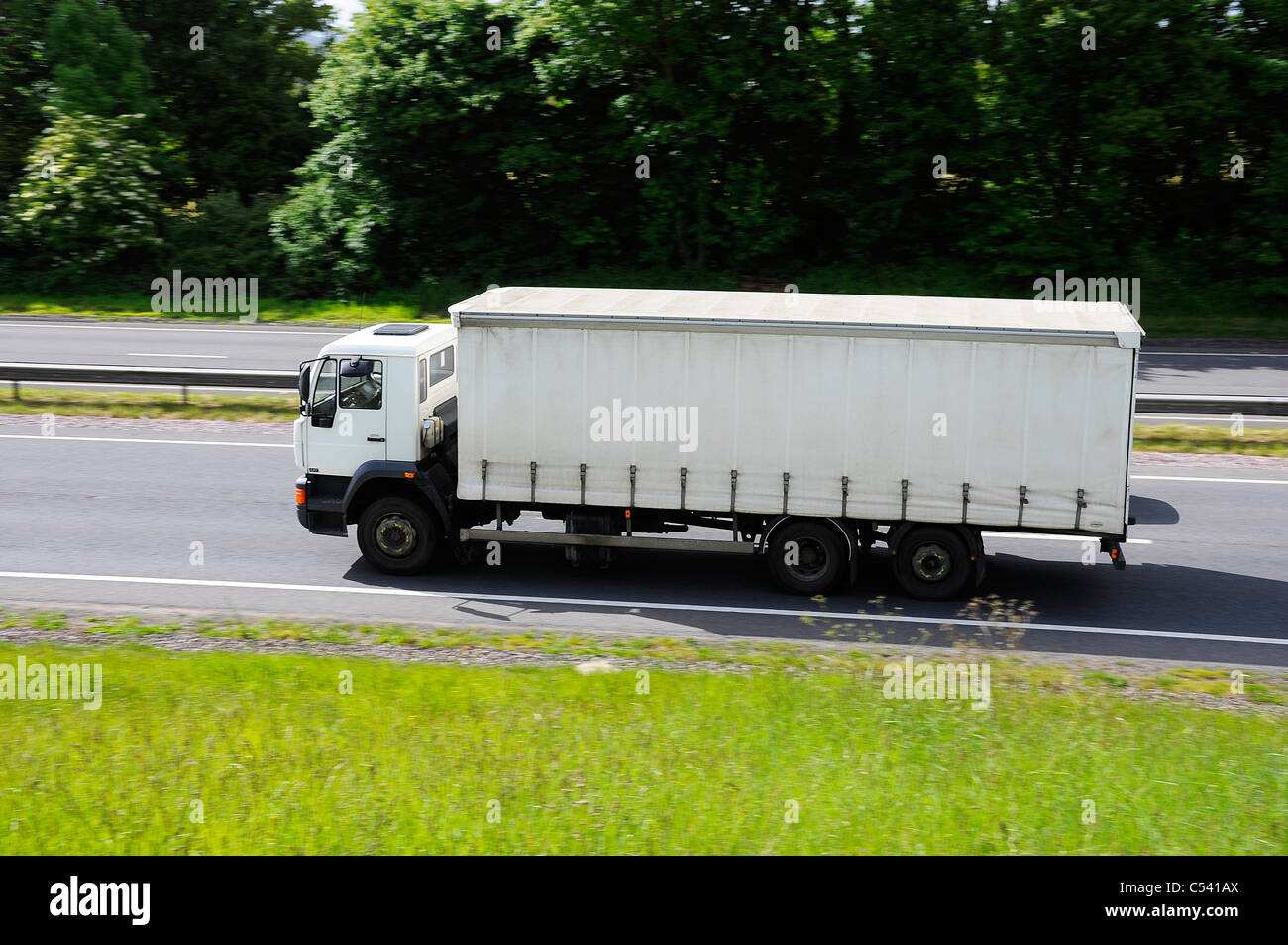 HGV Lorry with plain white curtain side trailer travelling on dual carriageway road. Stock Photo