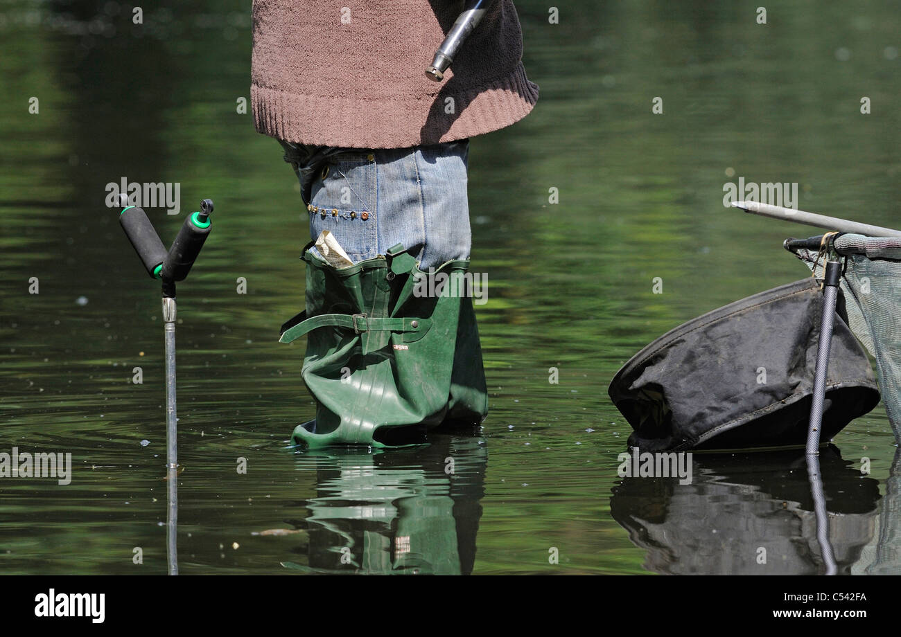 Fisherman wearing long green waders whilst fishing for fresh water fish on a shallow lake. Stock Photo