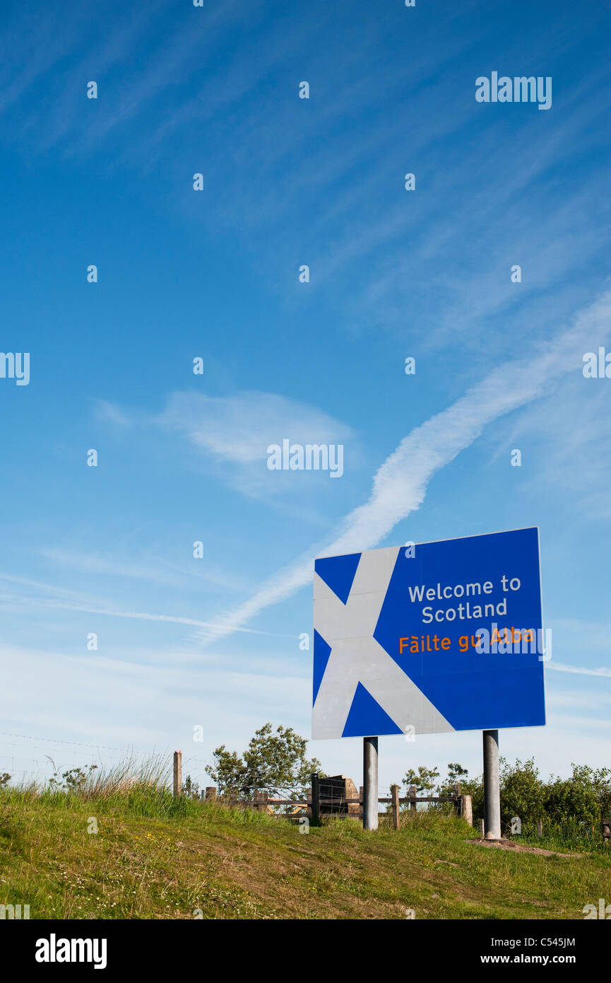 Scotland border sign at the Northumberland border in front of a white cross plane trail in the blue sky Stock Photo