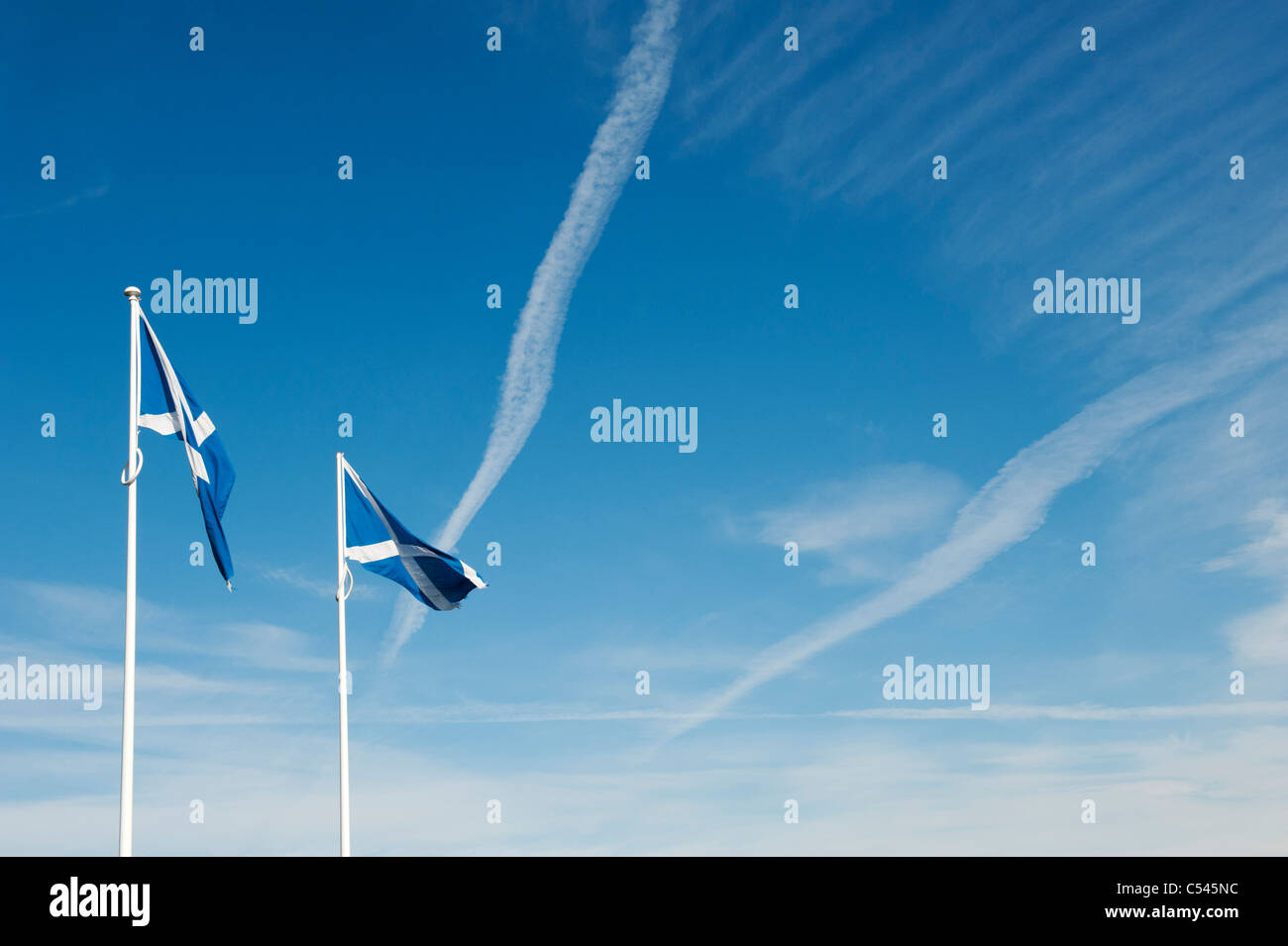 Scottish flags at the Northumberland / Scotland border in front of a white cross plane trail in the blue sky Stock Photo