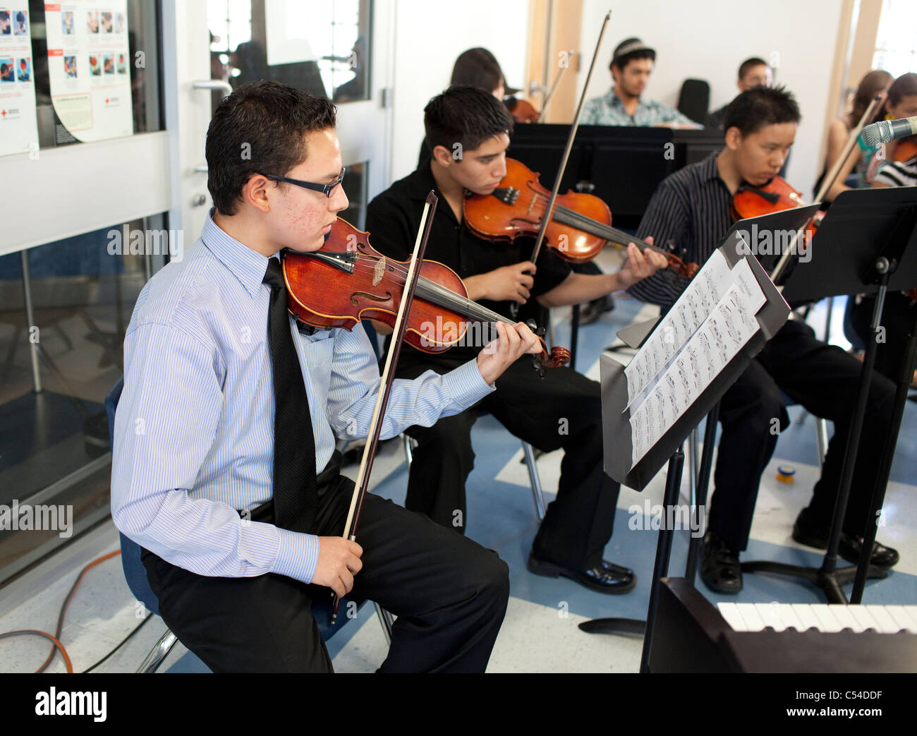 Students play stringed instruments, teacher conducts in orchestra class