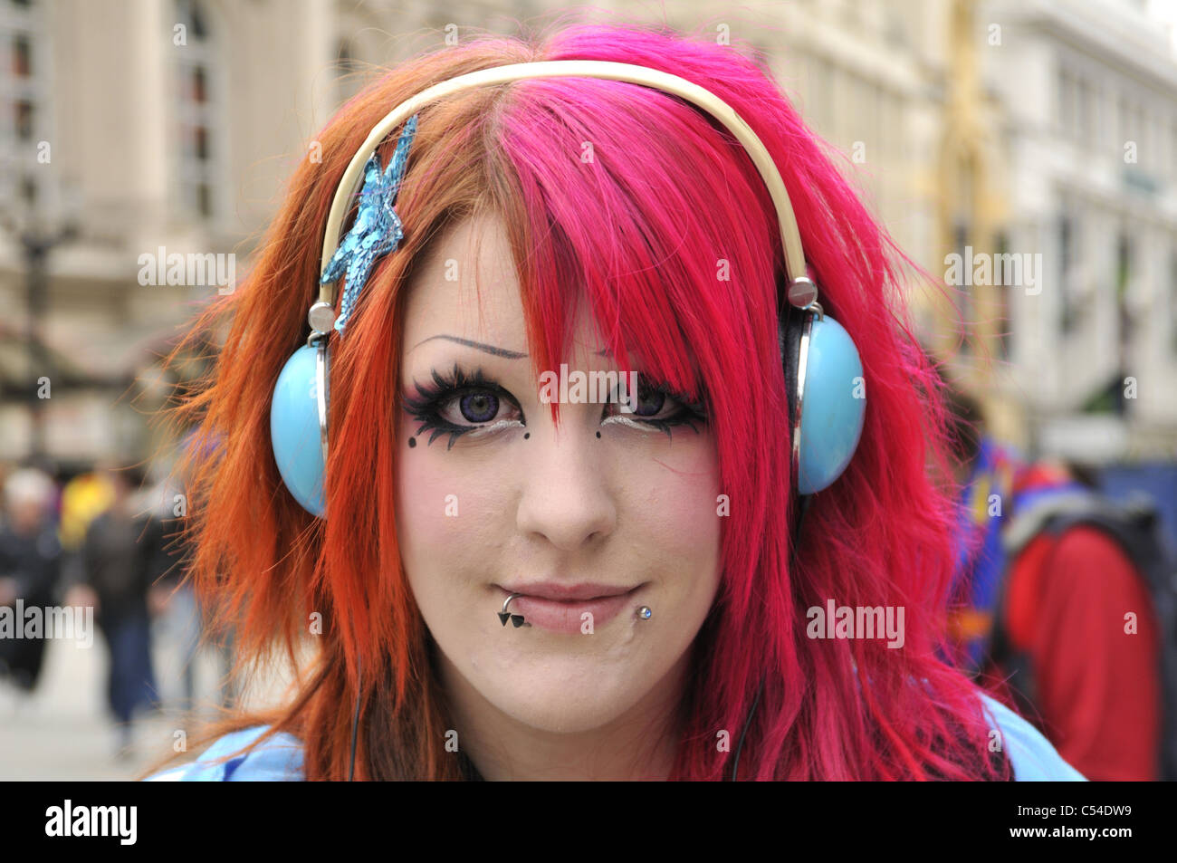 Girl with pink dyed hair, blue headphones and face piercings in