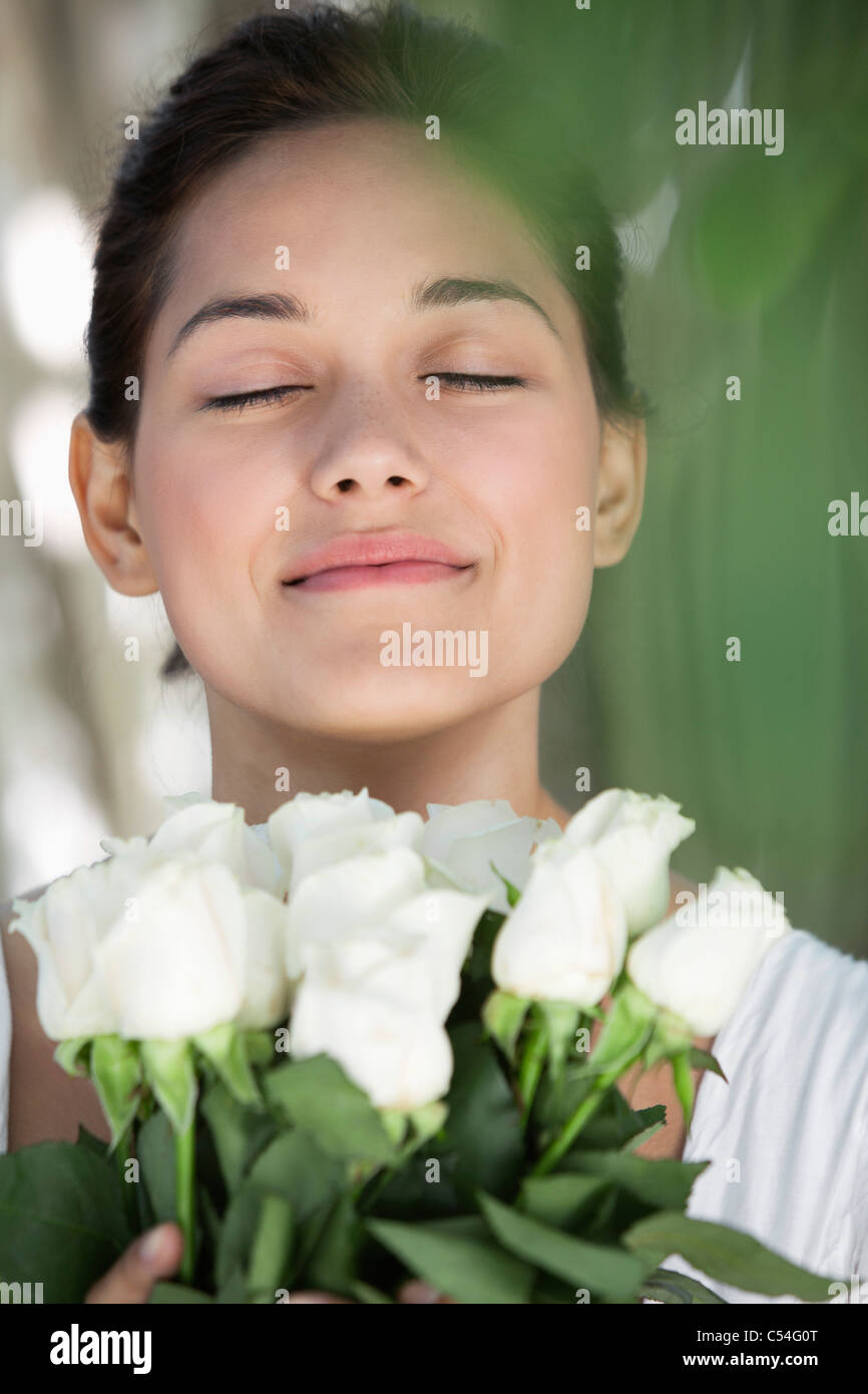 Beautiful young woman holding bunch of white flowers with her eyes ...