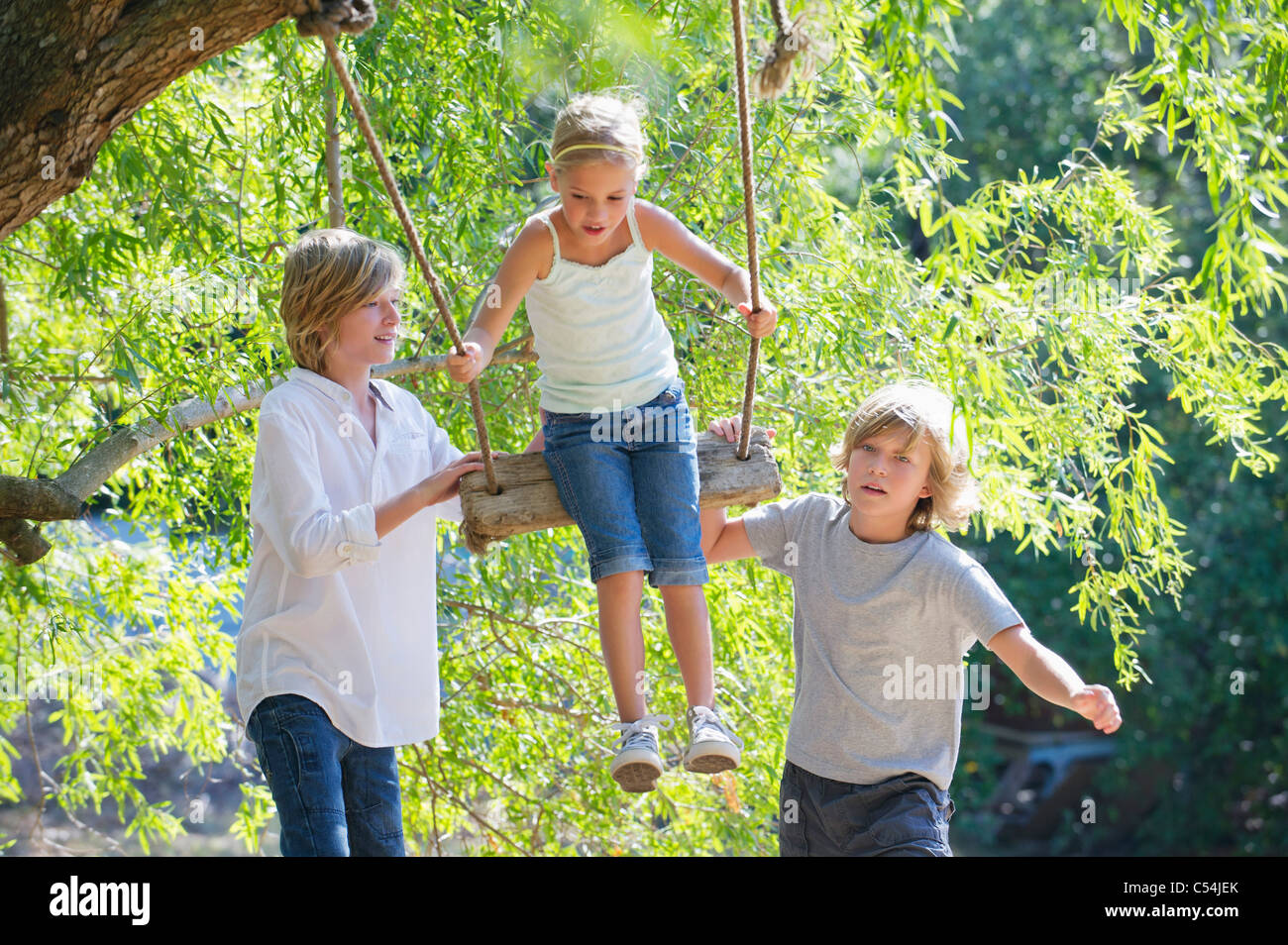 Smiling little siblings playing in tree swing Stock Photo