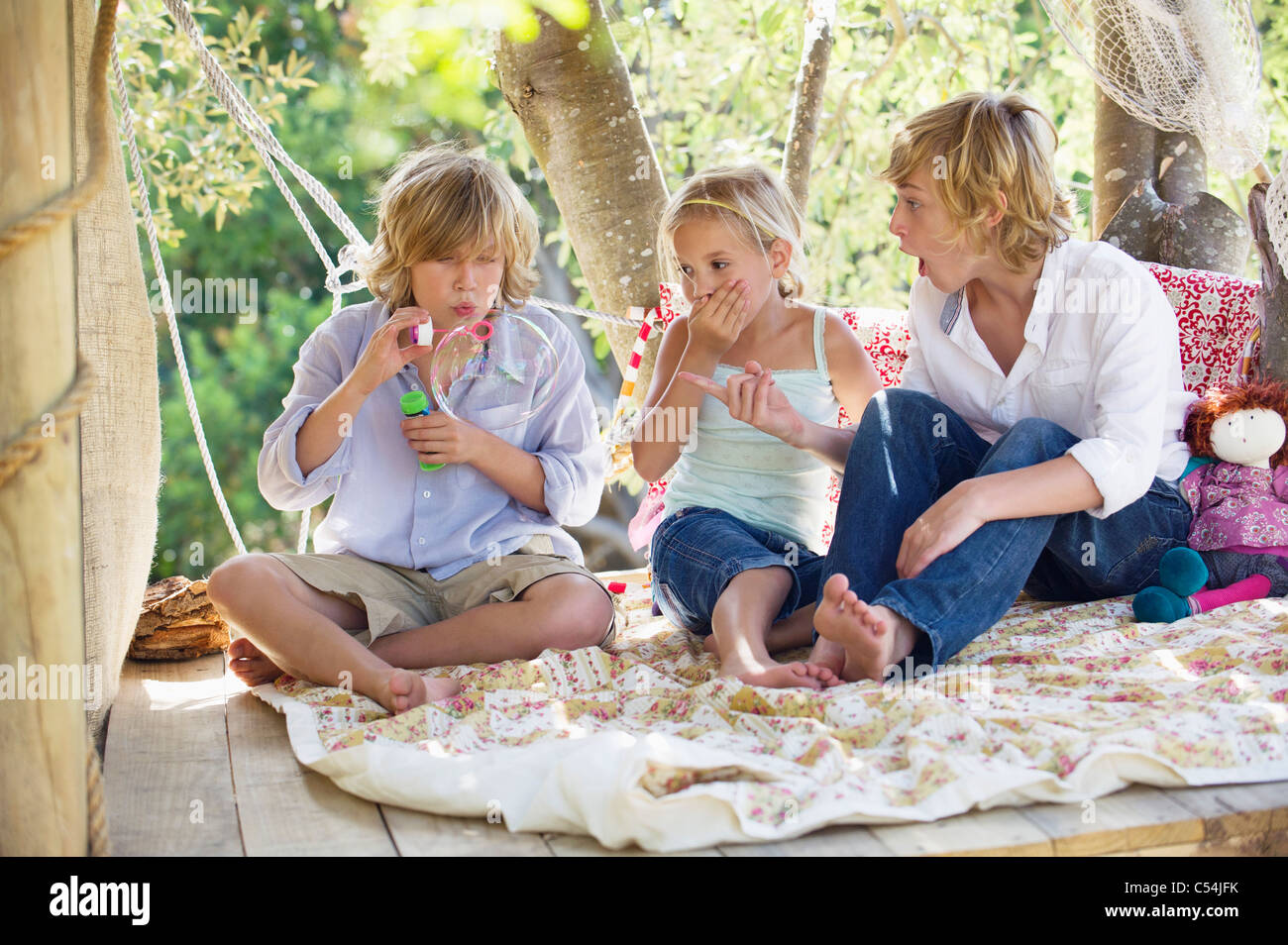 Children blowing bubble wand in tree house Stock Photo