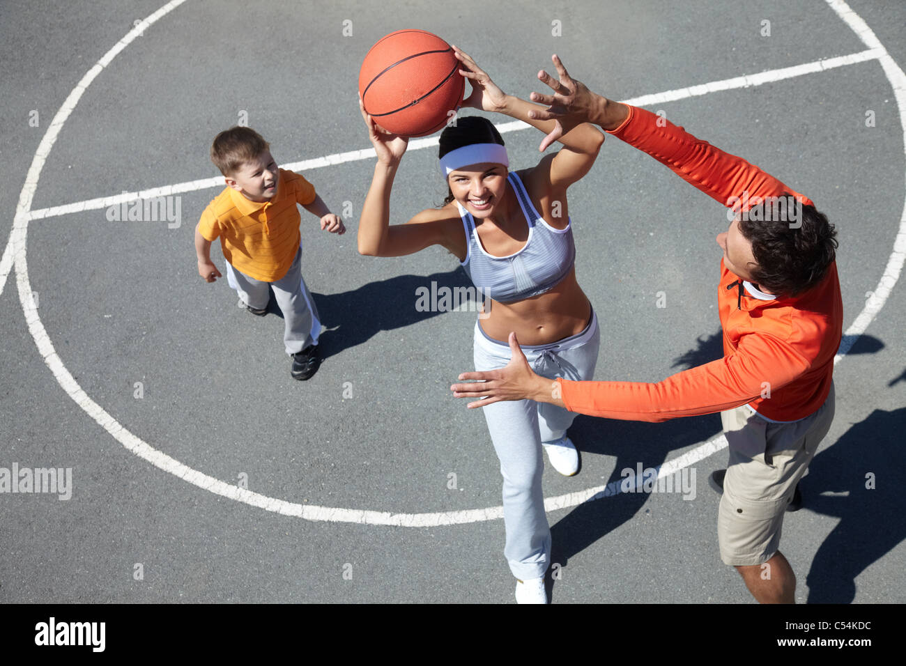 Image of happy female going to throw ball into basket with man and