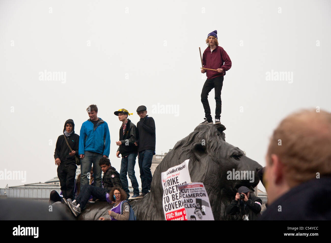Demonstrators against cuts on top of a lion in Trafalgar Square. Stock Photo