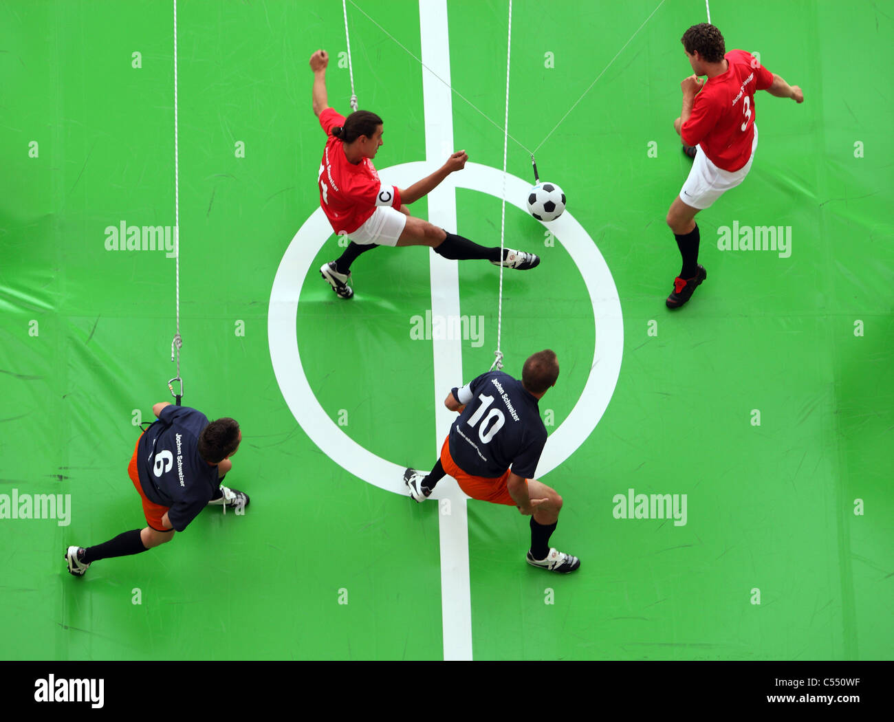 Football players hanging on ropes, playing football on a vertical field, Munich, Germany Stock Photo