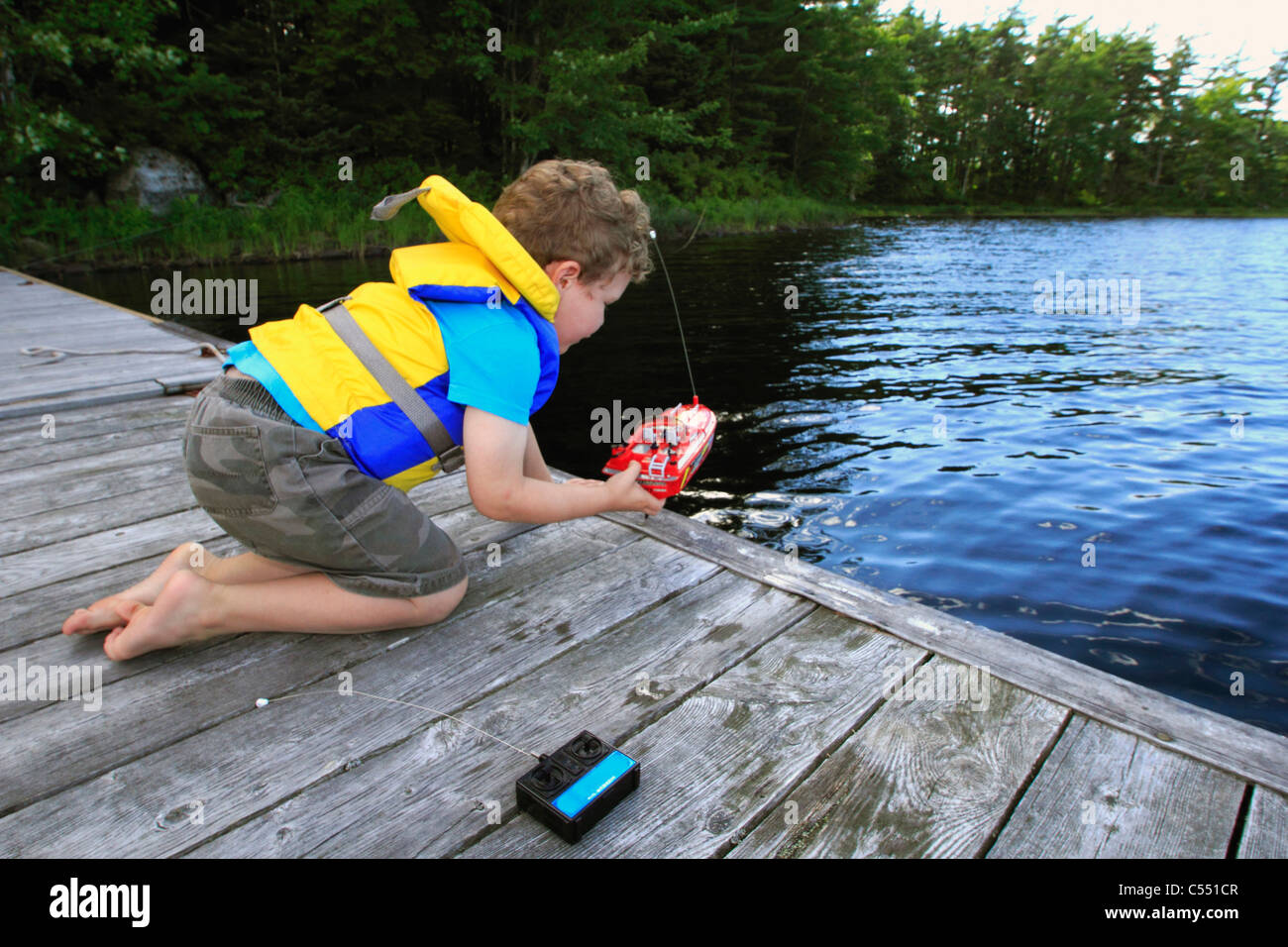 Boy playing with a remote controlled boat in a lake Stock Photo