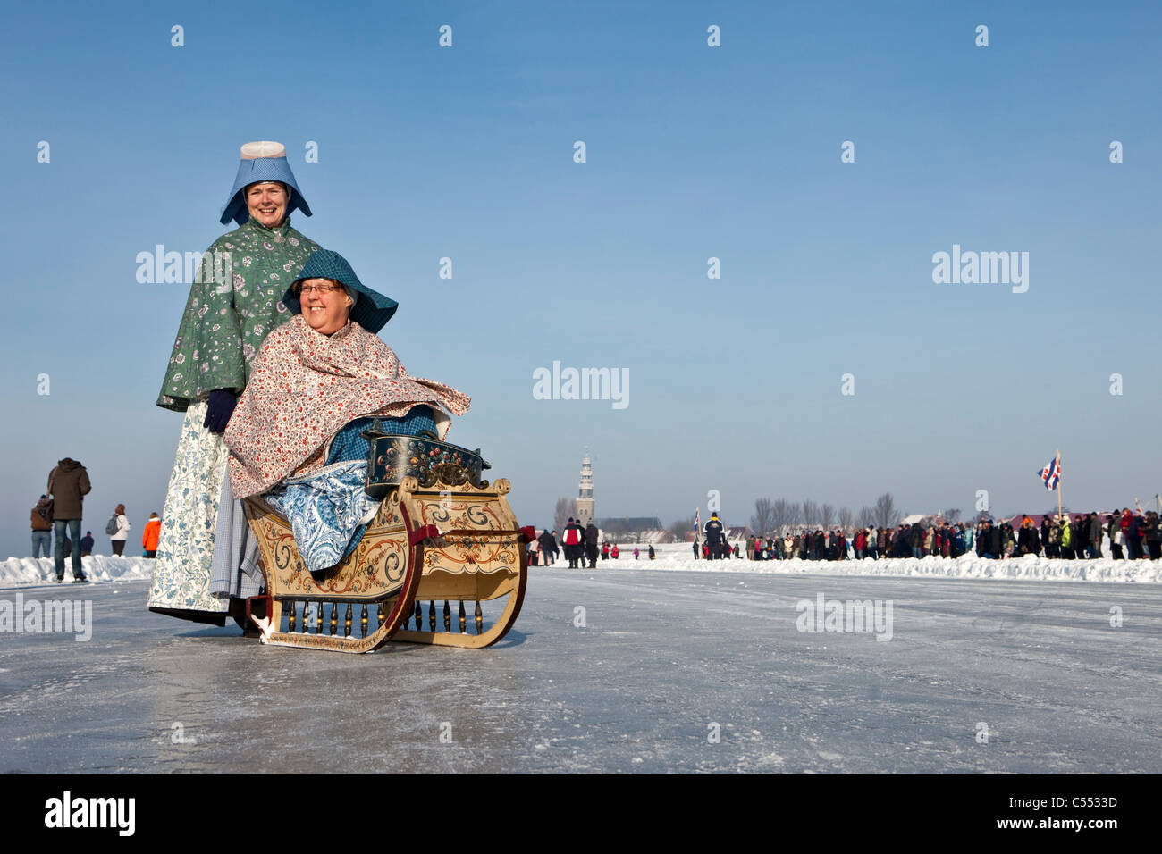 The Netherlands, Hindeloopen, Dutch capital of skating culture. Women dressed in traditional costume with sledge on ice. Stock Photo