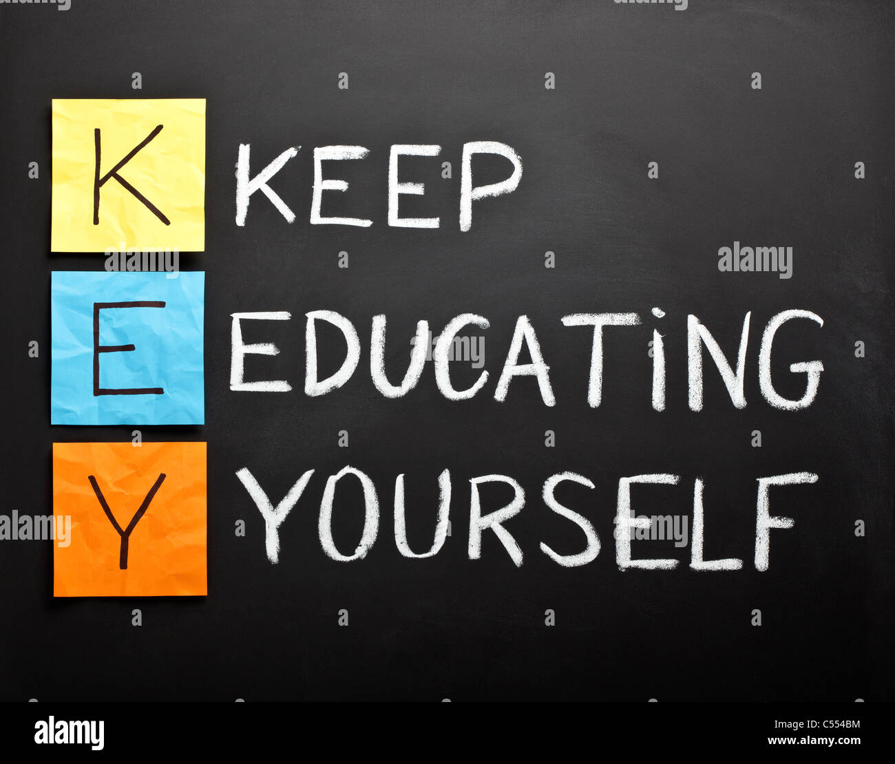 KEY acronym - KEEP EDUCATING YOURSELF. Educational concept with color sticky notes and white chalk handwriting on a blackboard. Stock Photo