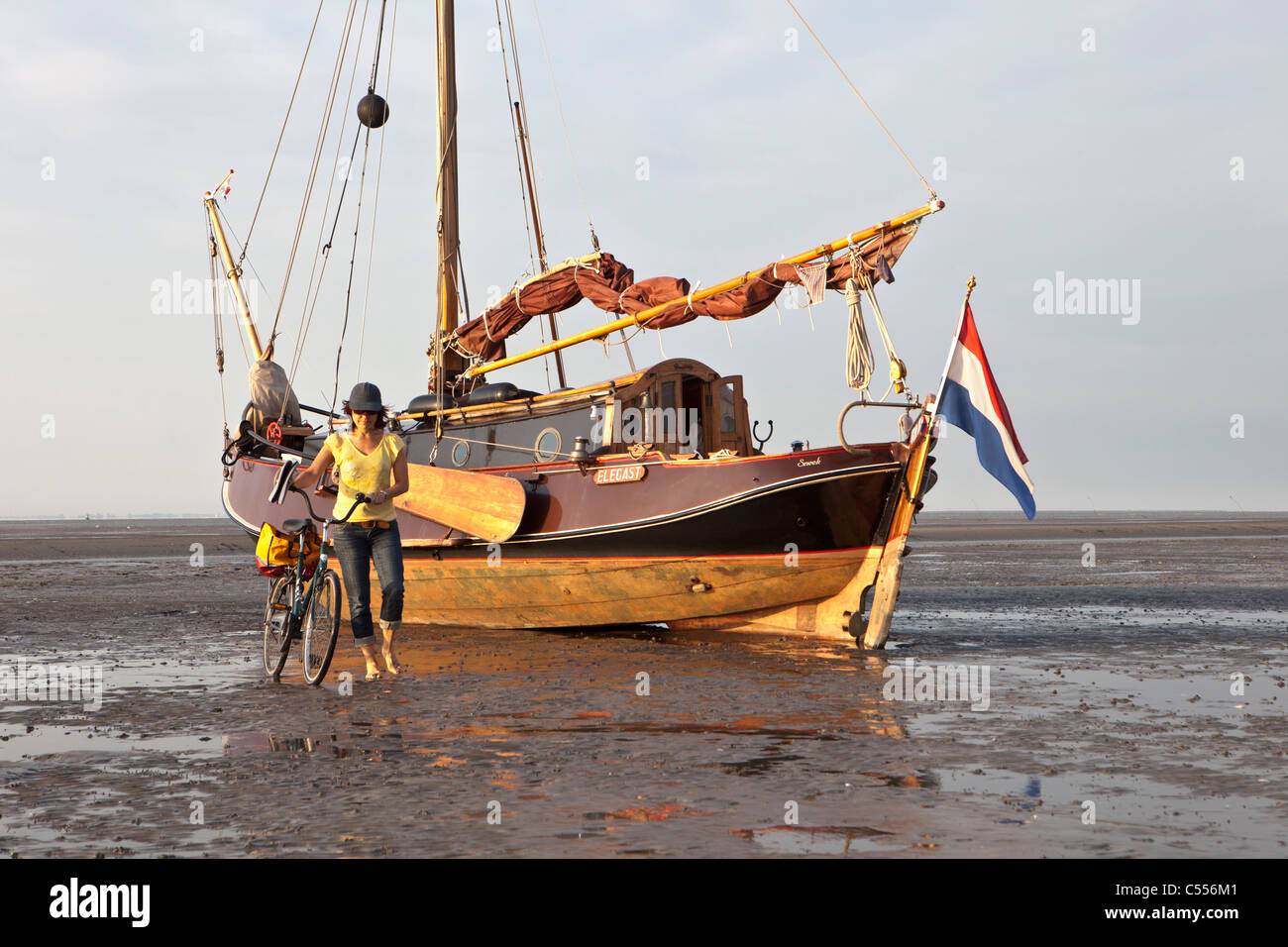 The Netherlands, Nes, Ameland Island, belonging to Wadden Sea Islands. Sailing boat on mud flat in harbour. Woman and bicycle. Stock Photo