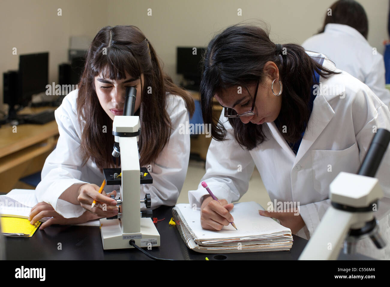female student  use microscopes in South Texas high school science classroom while classmate writes notes Stock Photo