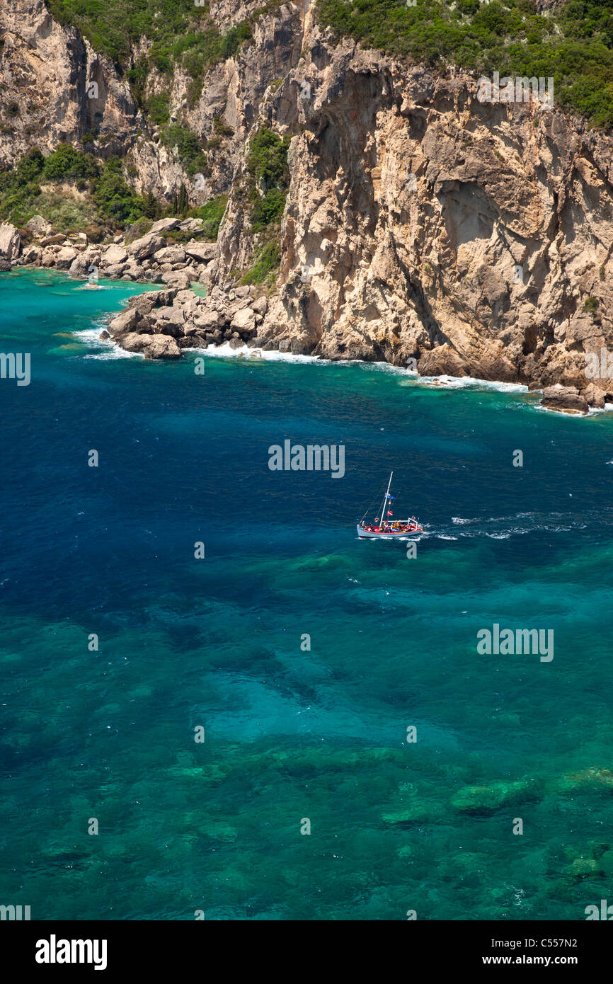 Tourist boat heads out to sea through clear blue and green water near Paleokastritsa, Corfu Greece Stock Photo