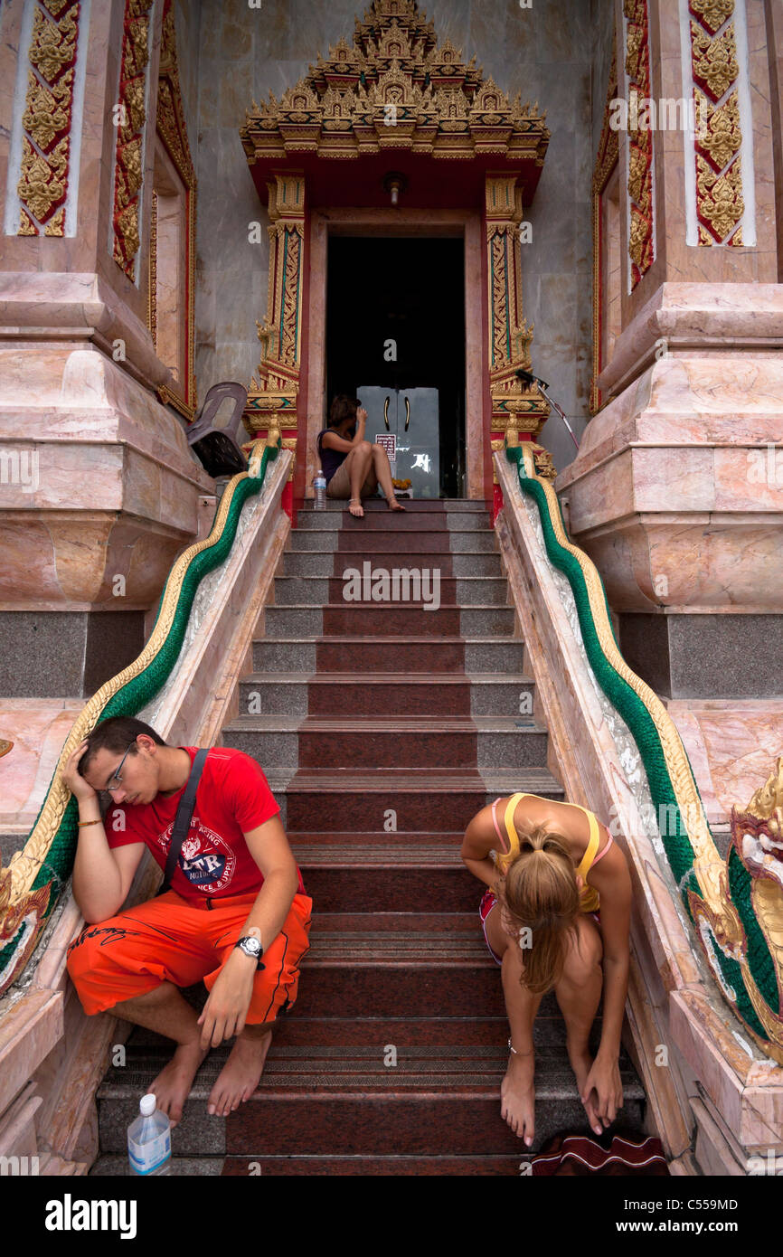 Tired European tourists resting at entrance to Wat Chalong - Buddhist temple in Phuket, Thailand. Stock Photo