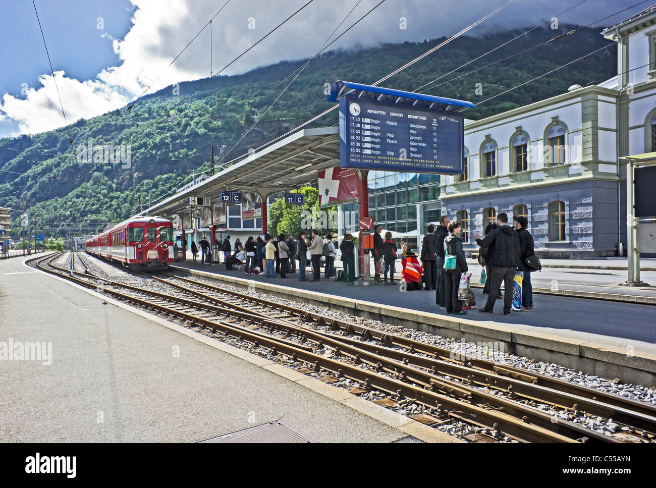 Passengers awaiting a Matterhorn Gotthard Bahn train on Platform 11 at Brig Railway Station in Brig Switzerland Stock Photo