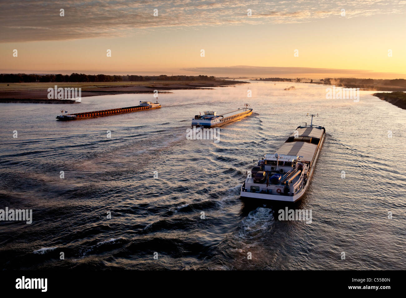 The Netherlands, Nijmegen, Cargo boats on Waal river. Sunrise. Stock Photo