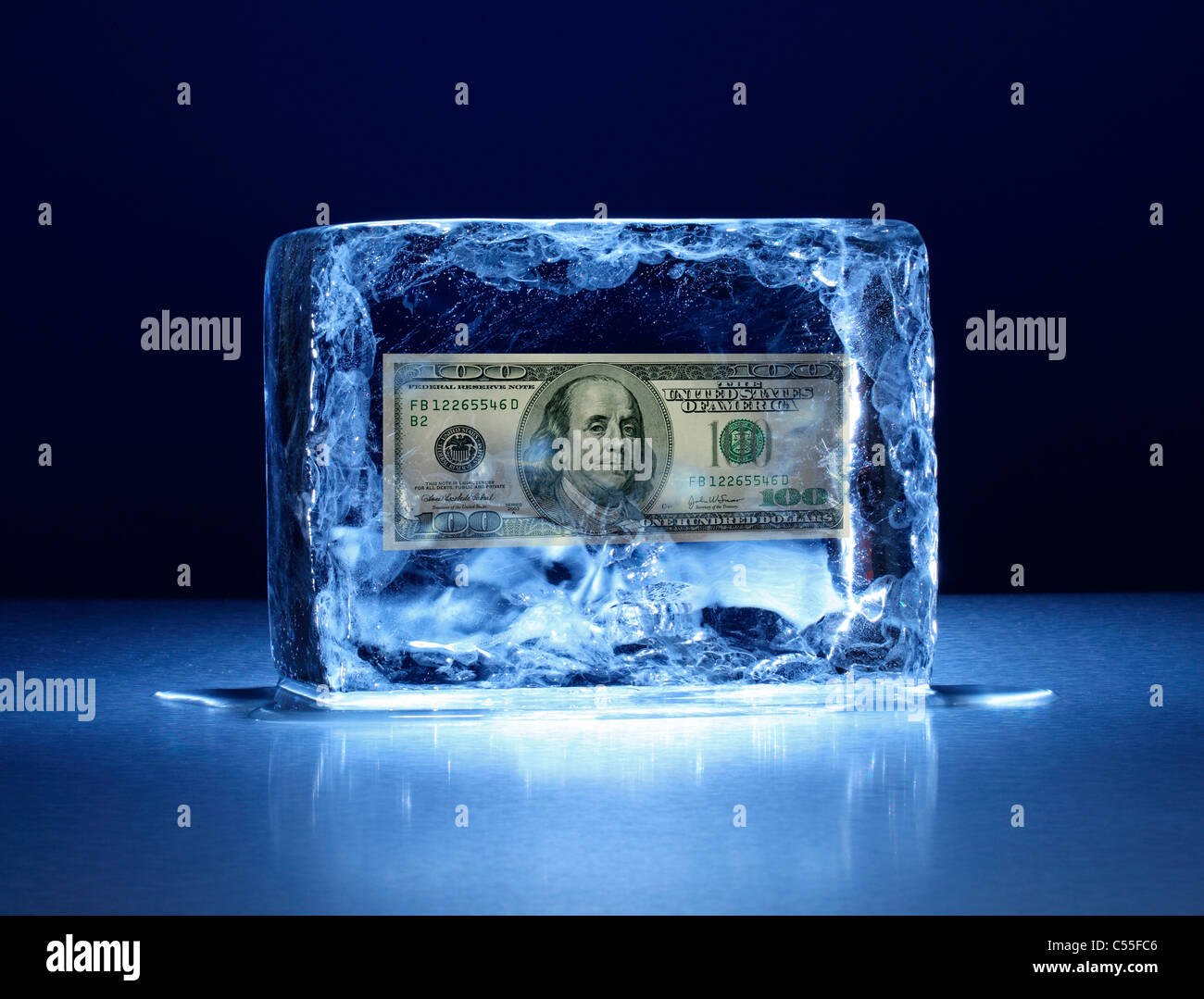 Large block of ice with one hundred dollar bill frozen inside stock