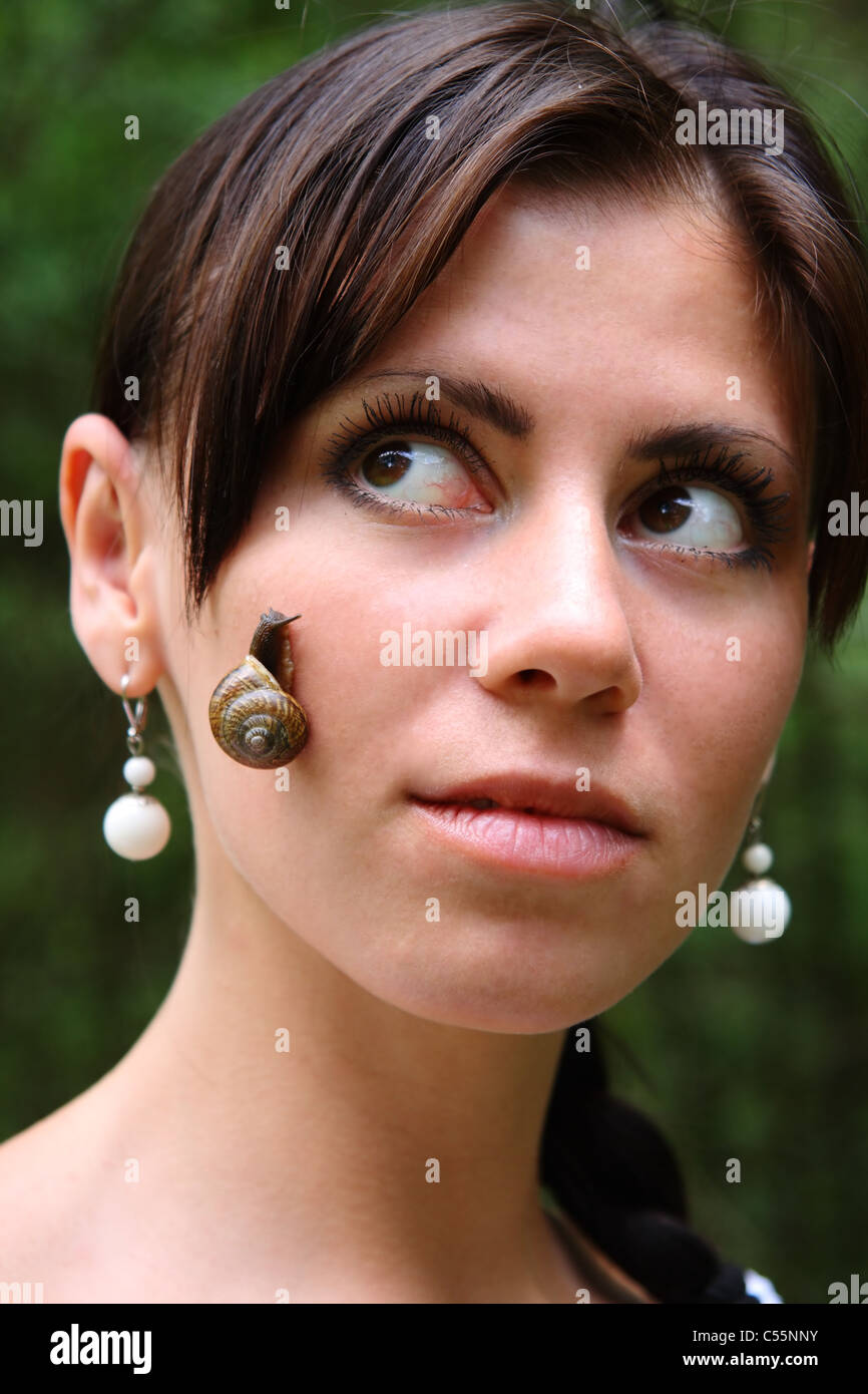 close-up of live garden snail on the face of young woman on green background Stock Photo