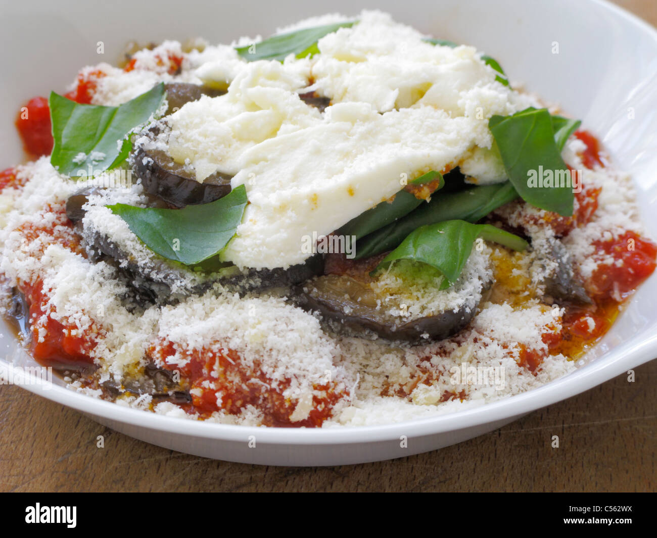 melanzane alla parmigiana individual portion in a white dish on of a wooden table kitchen chopping board prepared ready for oven Stock Photo